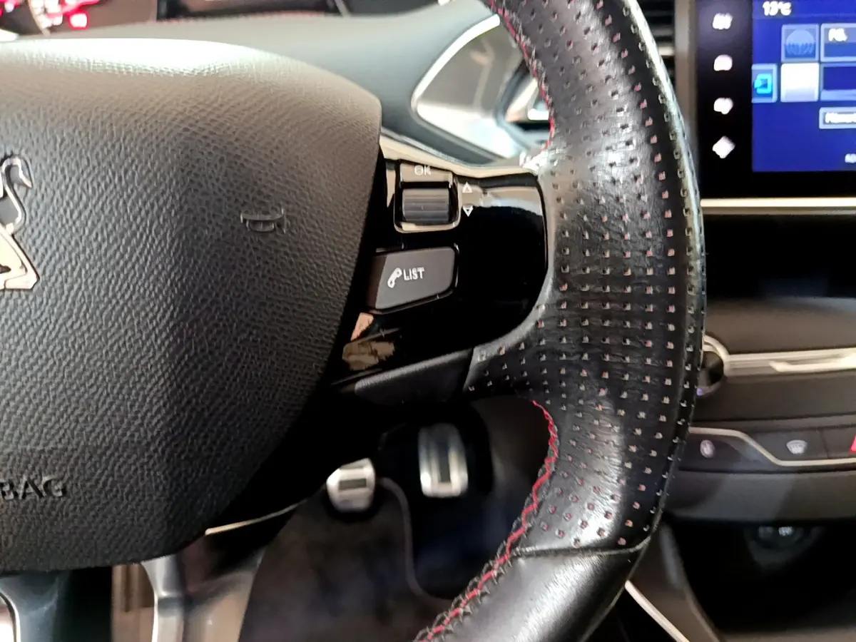 Gros plan sur le volant cuir perforé avec surpiqûres rouges de la Peugeot 308 GT Line 2016, tableau de bord tactile visible.