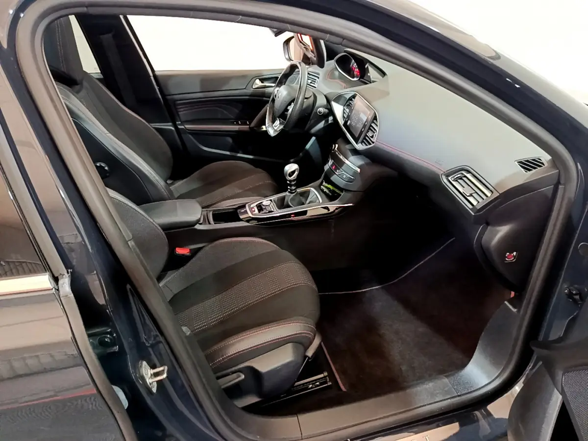Intérieur côté conducteur d'une Peugeot 308 gris foncé, volant cuir, console centrale avec boîte manuelle et écran tactile.