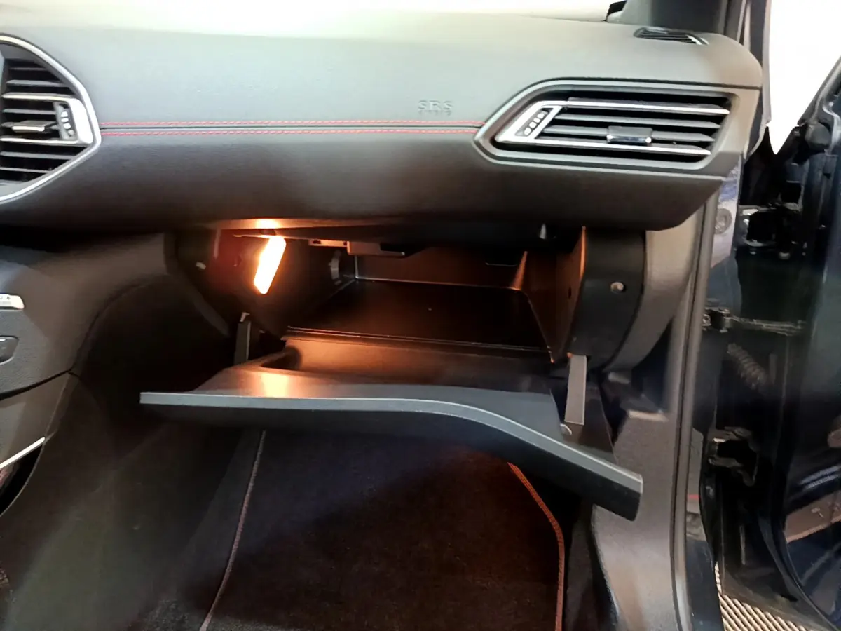 Gros plan sur la boîte à gants ouverte éclairée côté passager d'une Peugeot 308 gris foncé 2016.