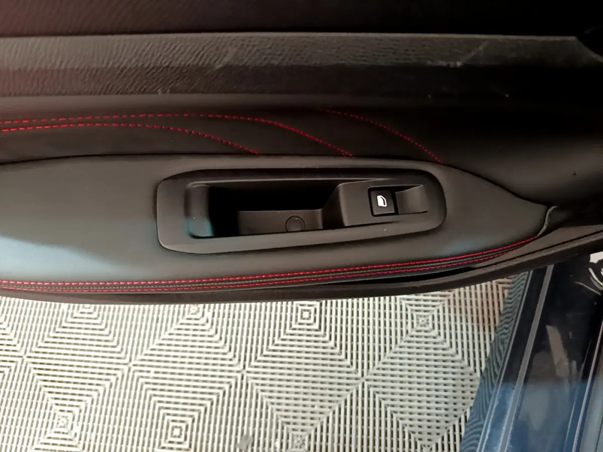 Poignée intérieure côté gauche avec bouton de verrouillage, sur porte en cuir noir à surpiqûres rouges du Peugeot 308 GT Line 2016.