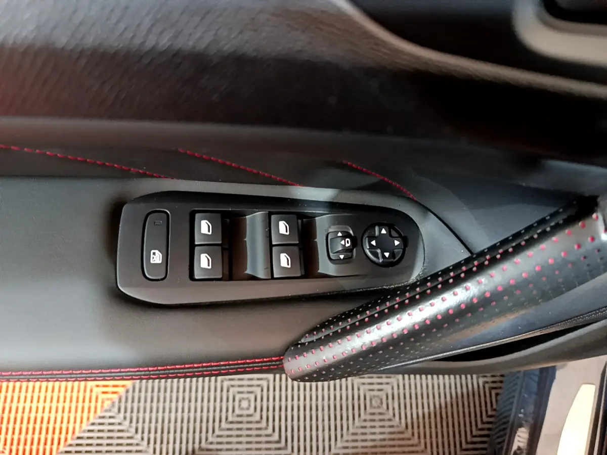 Commandes des vitres électriques et réglages des rétroviseurs sur la porte côté conducteur d'une Peugeot 308 gris foncé, avec surpiqûres rouges.