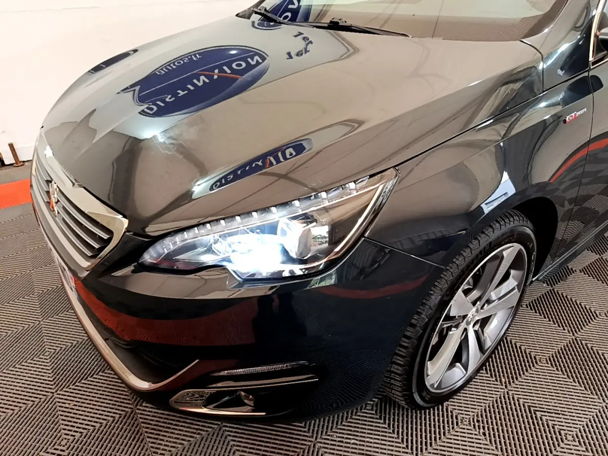 Vue 3/4 avant droit d'une Peugeot 308 gris foncé avec phares LED allumés et jantes alliage visibles.