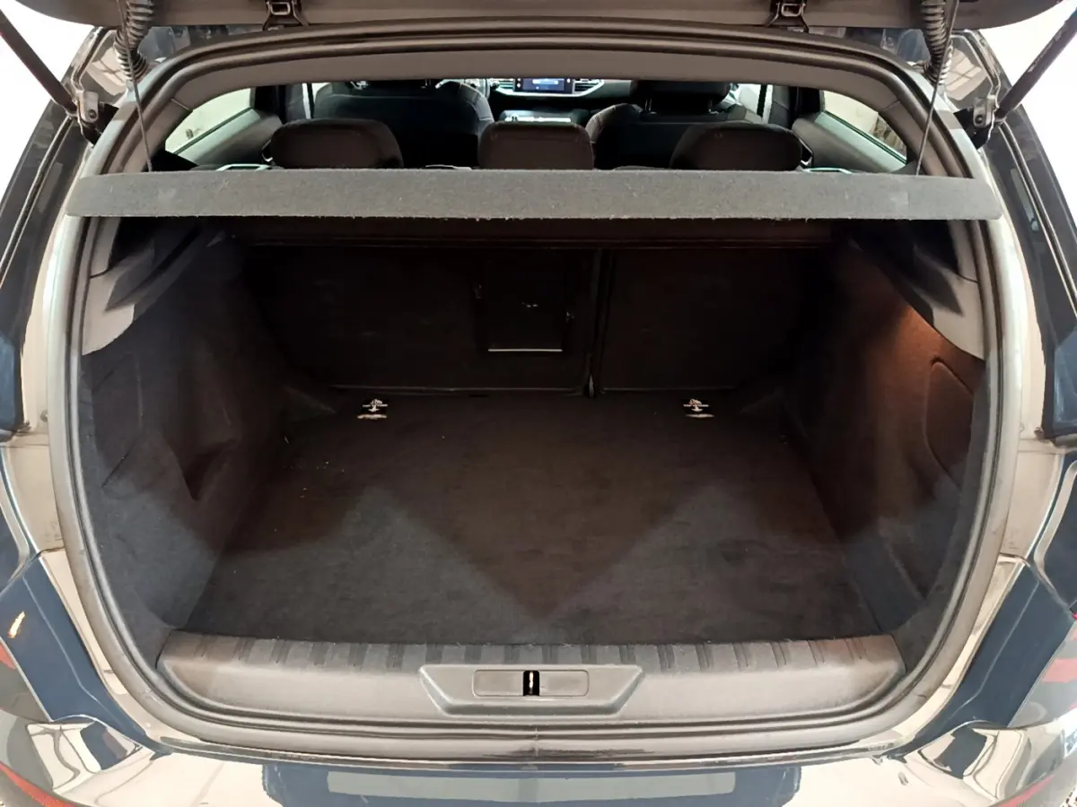 Coffre ouvert vu de l'arrière d'une Peugeot 308 gris foncé, montrant l'espace de chargement et la tablette cache-bagages.