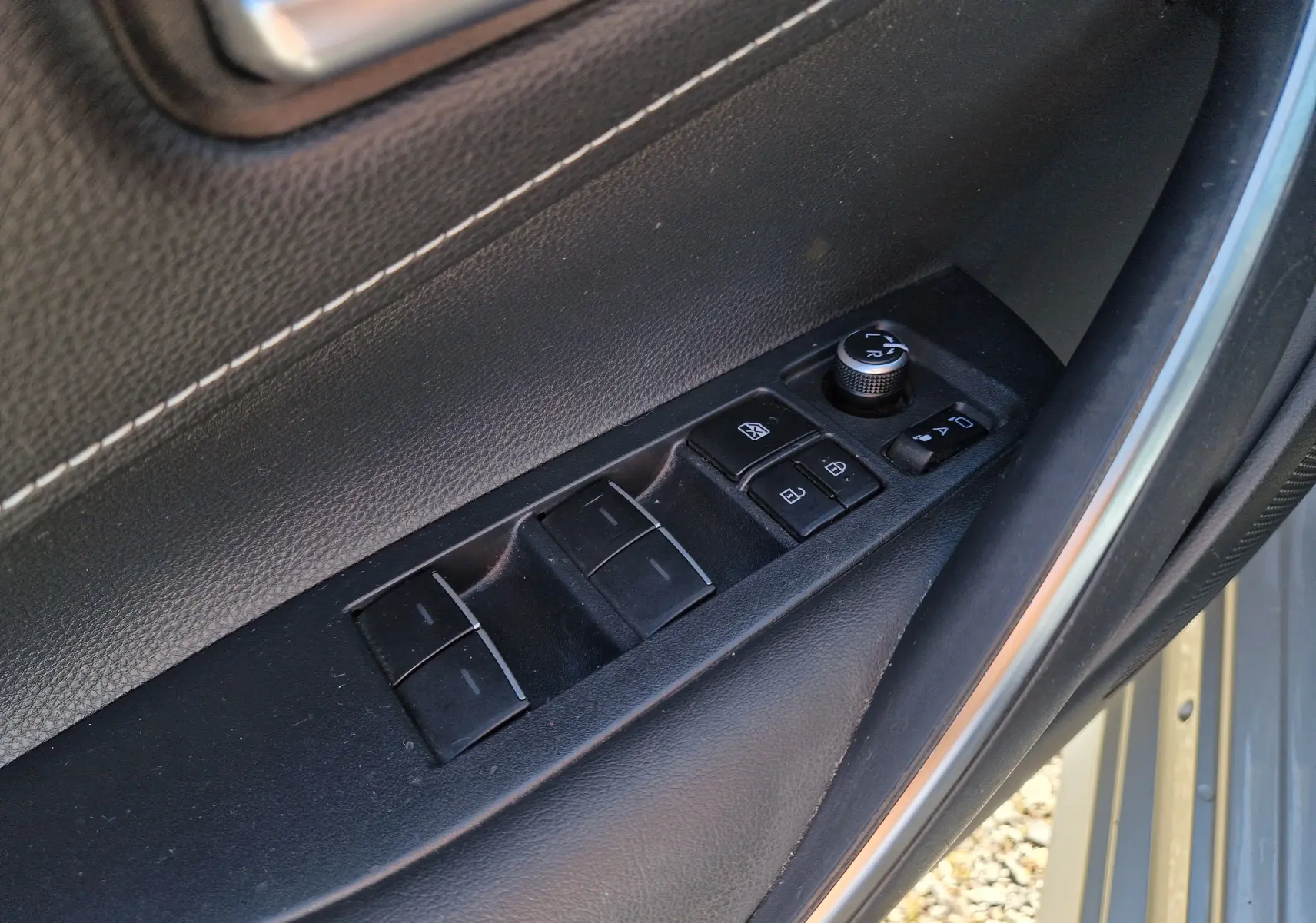 Gros plan sur les commandes de lève-vitres et rétroviseurs côté conducteur de la Toyota Corolla hybride gris clair 2019.