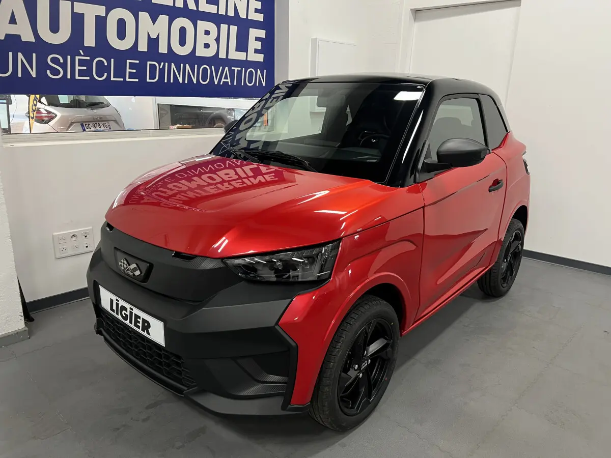 Vue 3/4 avant droite d'une LIGIER JS50 BEV 8KWH ELITE rouge avec toit noir et jantes alu noires en intérieur showroom.