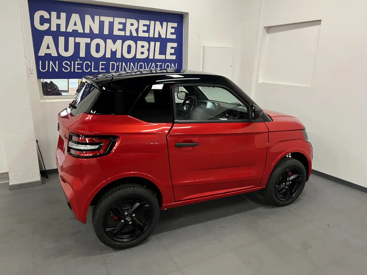 Vue de profil droit d'une LIGIER JS50 BEV 8KWH ELITE rouge avec toit noir et jantes alu noires en intérieur showroom.