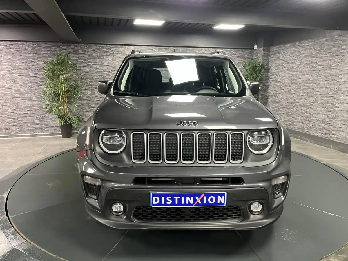 Vue frontale d'un Jeep Renegade gris métallisé avec calandre noire et feux LED ronds en intérieur showroom.