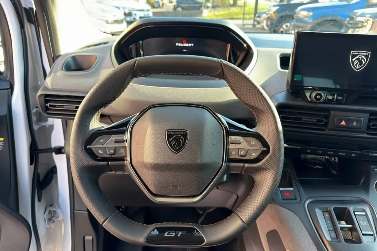 Vue intérieure centrée sur le volant cuir multifonctions du Peugeot Rifter GT Plus 2025, avec écran tactile et tableau de bord numérique.