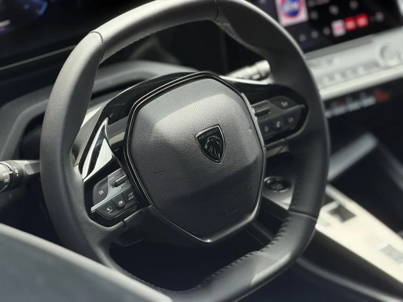 Gros plan sur le volant cuir noir de la Peugeot 308 SW 2025 avec commandes intégrées et logo lion central.