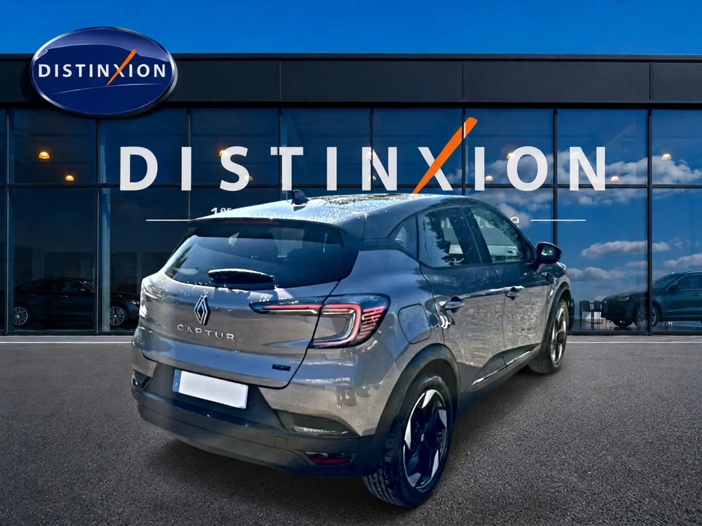 Vue 3/4 arrière droite d'un Renault Captur gris Cassiopée 2026 devant une vitrine Distinxion.