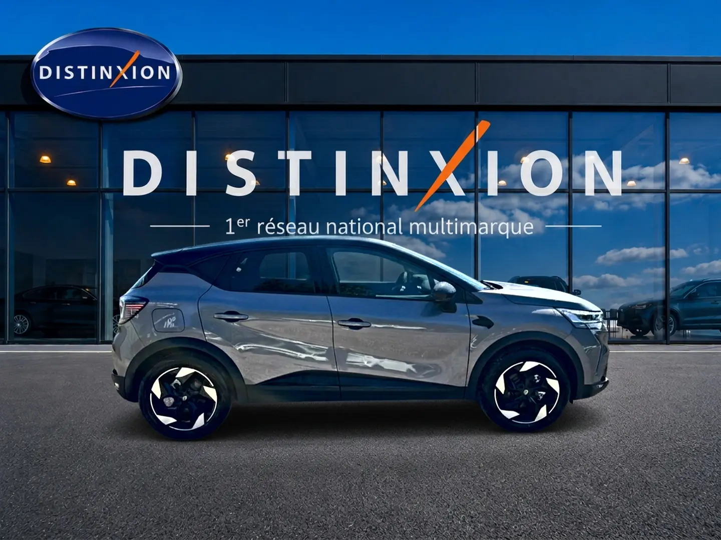 Renault Captur gris cassiopée en profil droit, avec jantes noires et toit noir, devant une vitrine Distinxion.