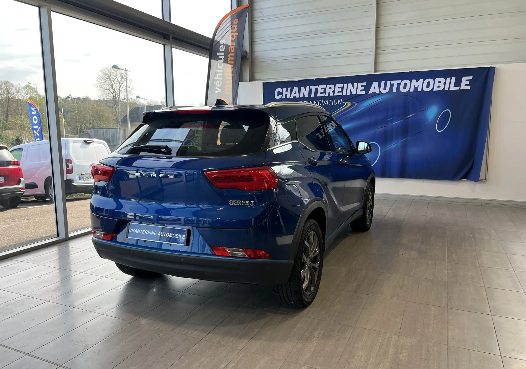 Vue 3/4 arrière droite du SUV électrique SERES 3 bleu astral métallisé dans un showroom lumineux.