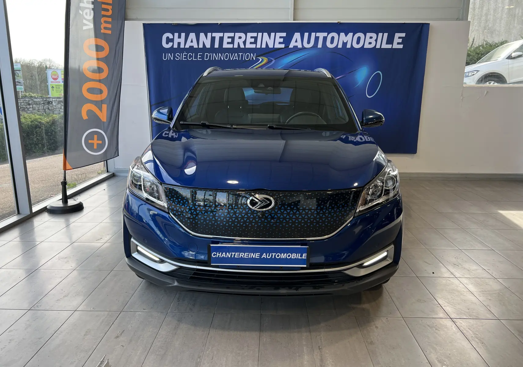 Vue frontale d'un SUV SERES 3 Electric bleu astral métallisé avec calandre noire à motifs triangulaires et phares LED.