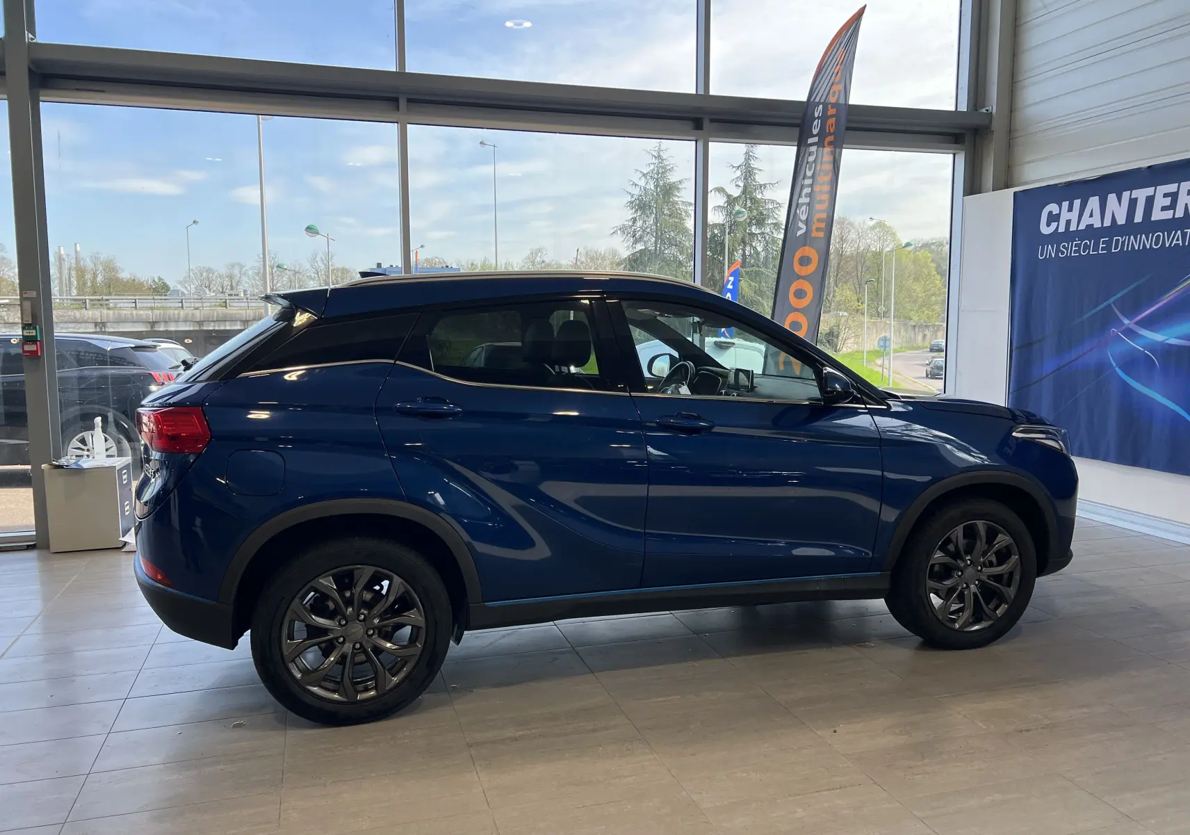 Vue de profil côté gauche du SUV électrique SERES 3 Luxe en bleu astral métallisé dans un showroom lumineux.