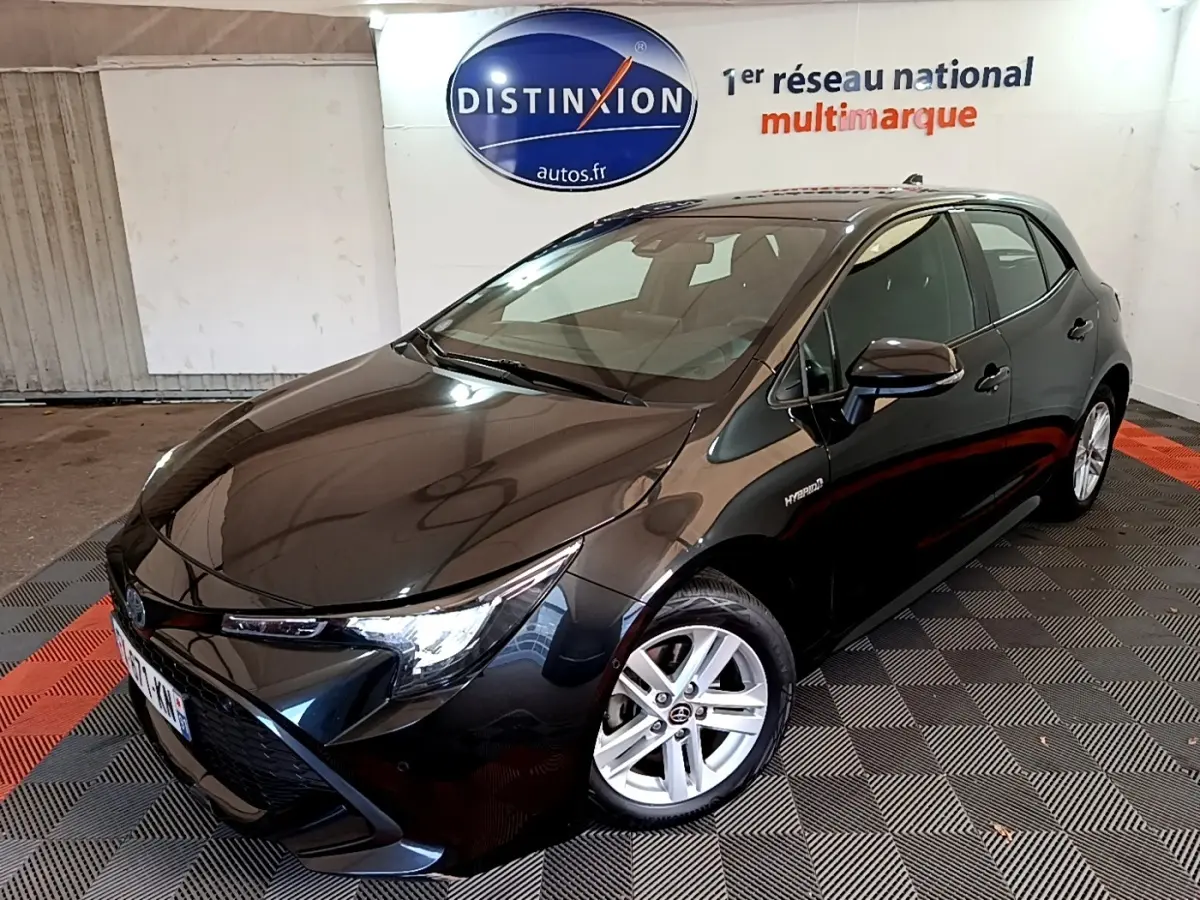 Toyota Corolla hybride noire vue en 3/4 avant droit dans un showroom avec jantes argentées et logo Distinxion en arrière-plan