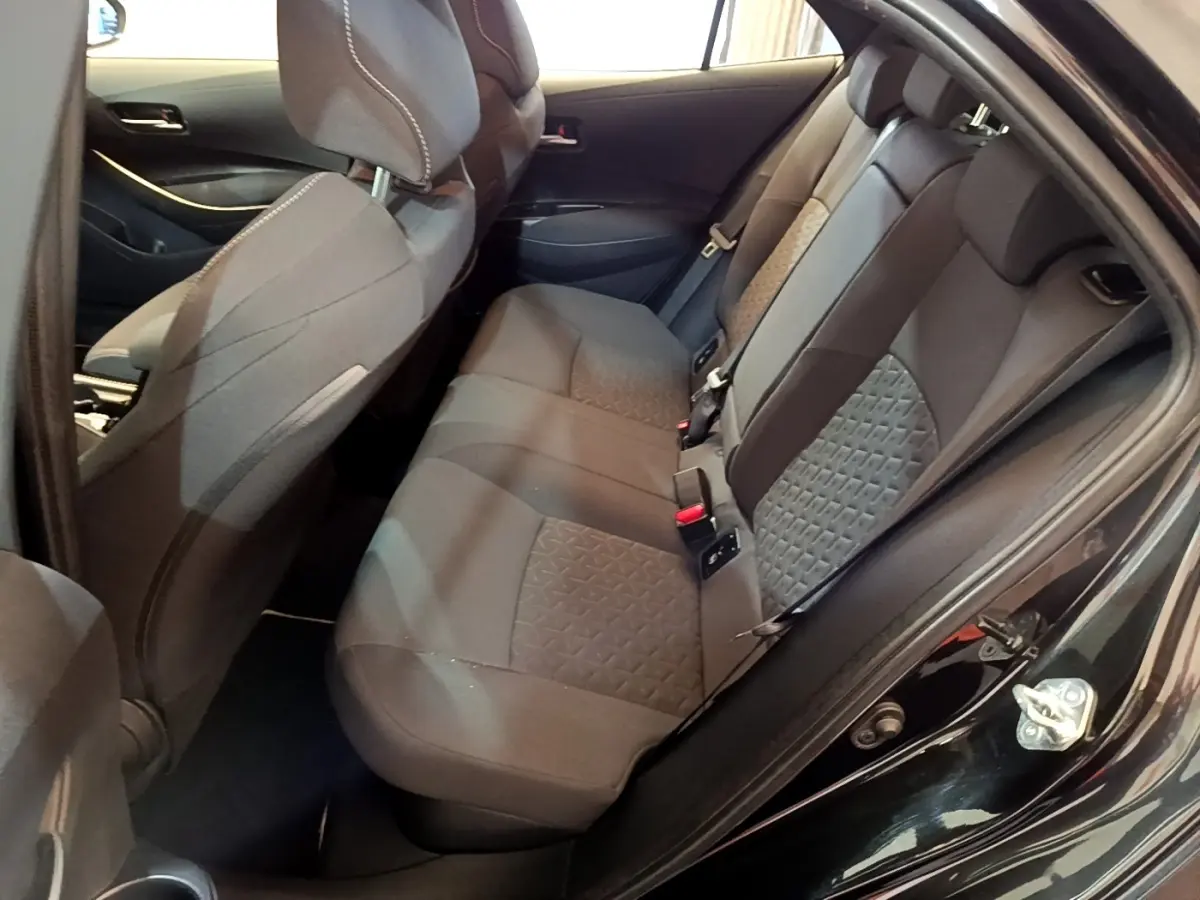 Vue intérieure côté gauche montrant la banquette arrière noire de la Toyota Corolla Hybride 2021 avec sièges tissu et ceintures visibles.