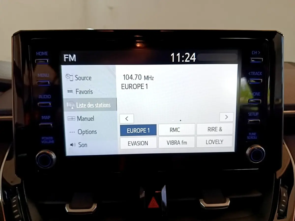 Écran tactile central de la Toyota Corolla hybride noire 2021 affichant la liste des stations radio FM à 11h24.