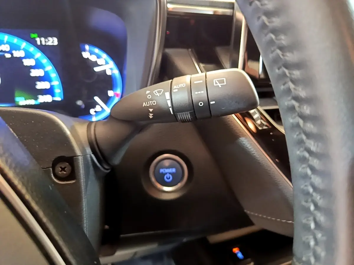 Gros plan sur la manette d’essuie-glace à gauche du volant cuir noir, avec bouton démarrage bleu illuminé en arrière-plan.