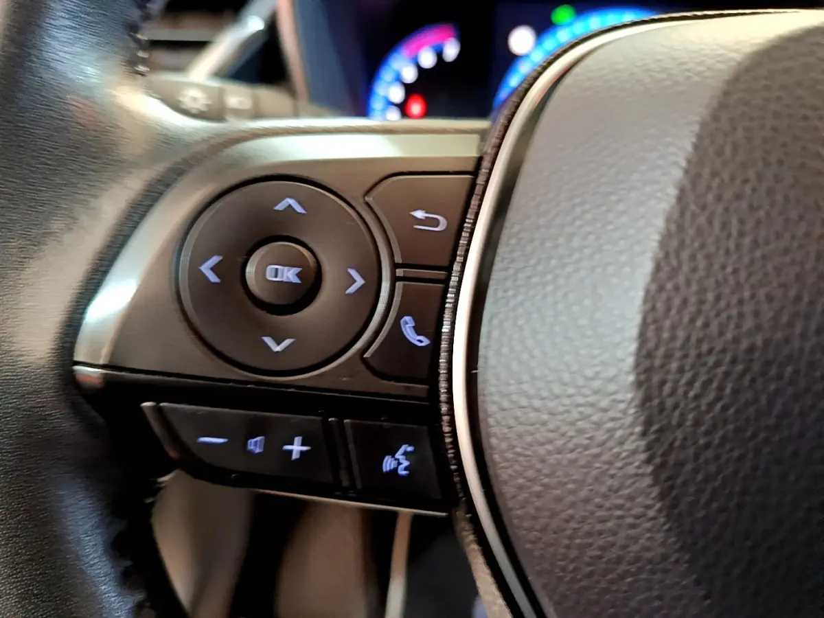 Gros plan sur les commandes gauche du volant en cuir noir de la Toyota Corolla hybride 2021 avec boutons rétroéclairés.