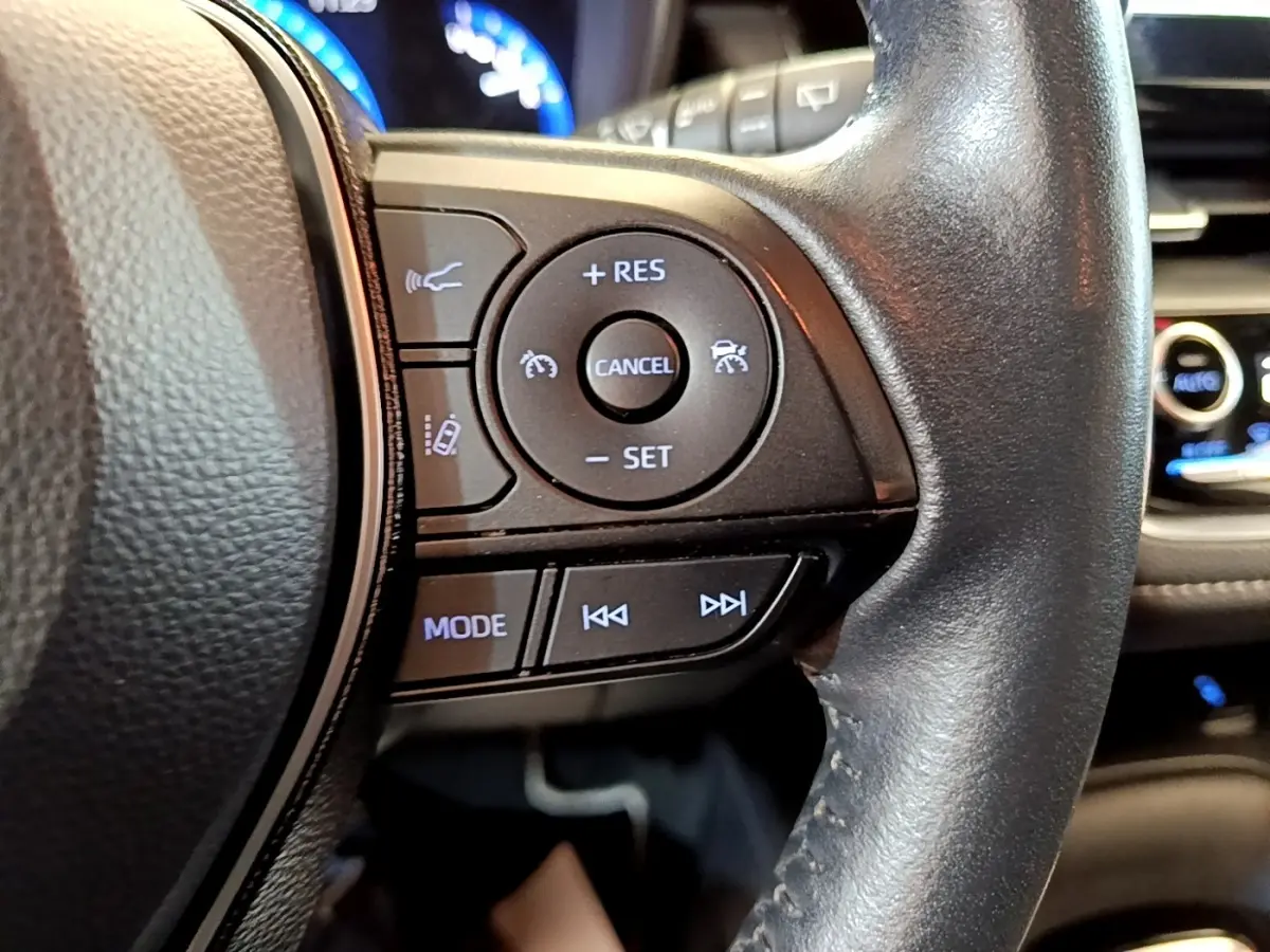 Gros plan sur les commandes du volant cuir à droite de la Toyota Corolla hybride noire, avec affichage numérique en arrière-plan.