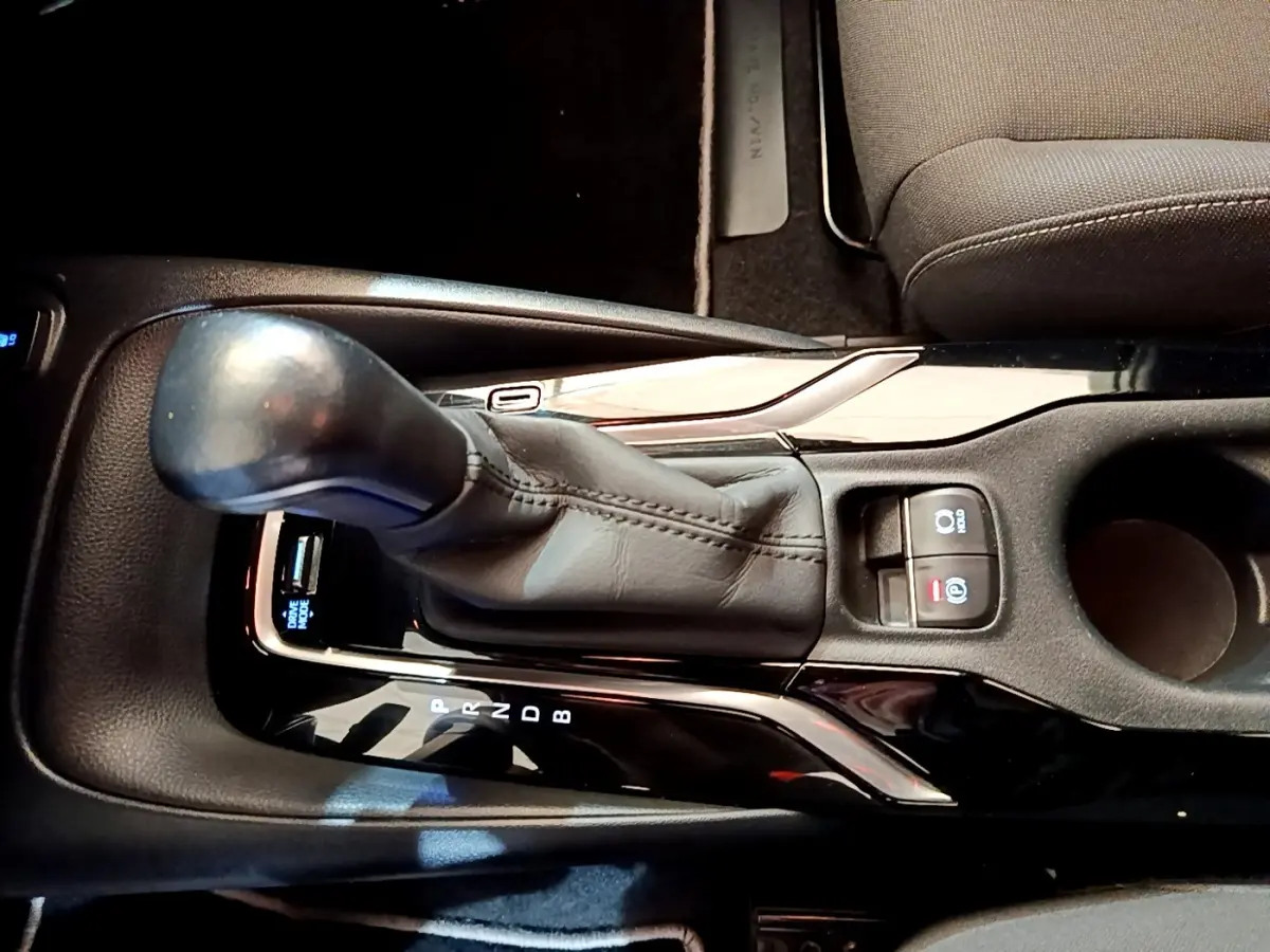 Gros plan sur la console centrale noire de la Toyota Corolla hybride 2021, avec levier de vitesse automatique et commandes électroniques.