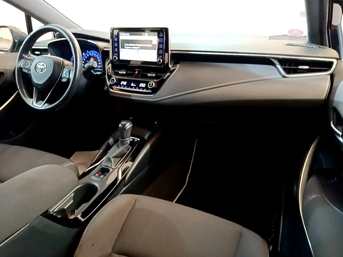 Intérieur noir de la Toyota Corolla Hybride 2021, vue du tableau de bord et console centrale avec écran tactile et volant cuir.