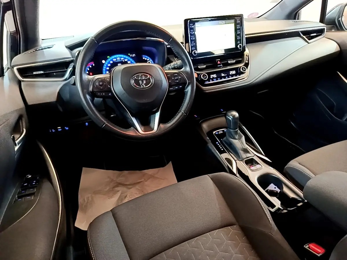 Intérieur noir de la Toyota Corolla Hybride 2021, vue du poste de conduite avec écran tactile central et volant cuir.