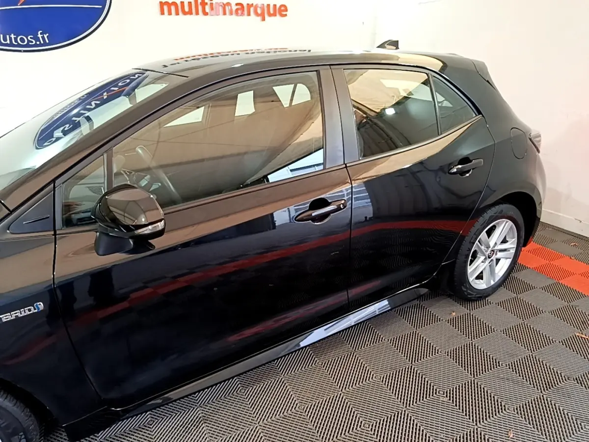 Profil côté gauche de la Toyota Corolla hybride noire 2021, mettant en valeur les jantes alliage et le badge Hybrid.