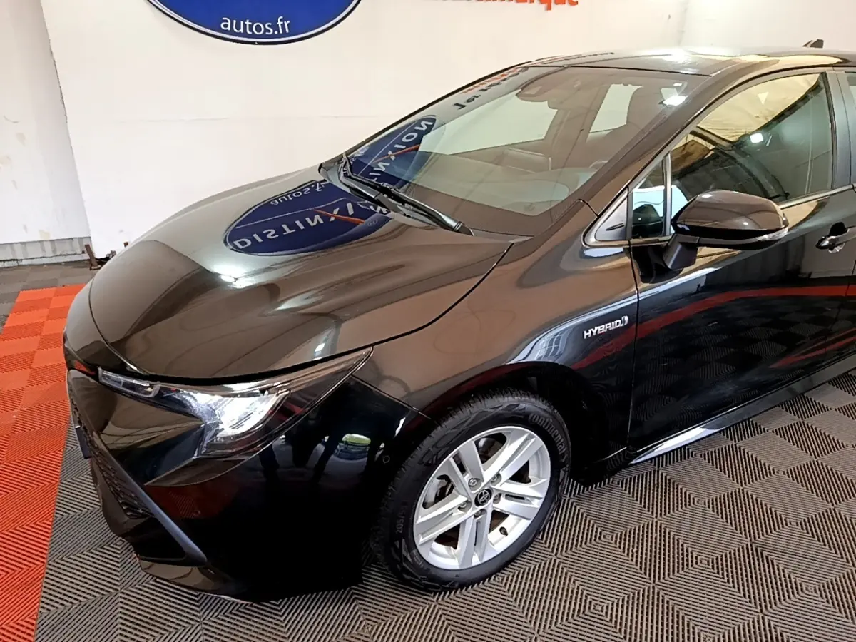Toyota Corolla hybride noire vue de 3/4 avant droit, mettant en valeur ses phares LED et la mention Hybrid sur la portière.