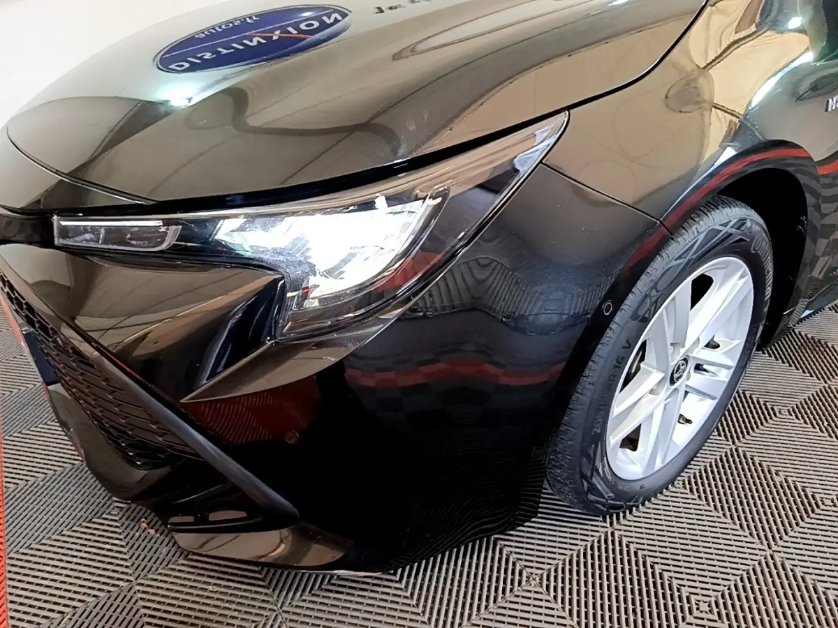 Gros plan sur l'avant droit noir brillant de la Toyota Corolla hybride 2021 avec phare LED allumé et jante argentée.