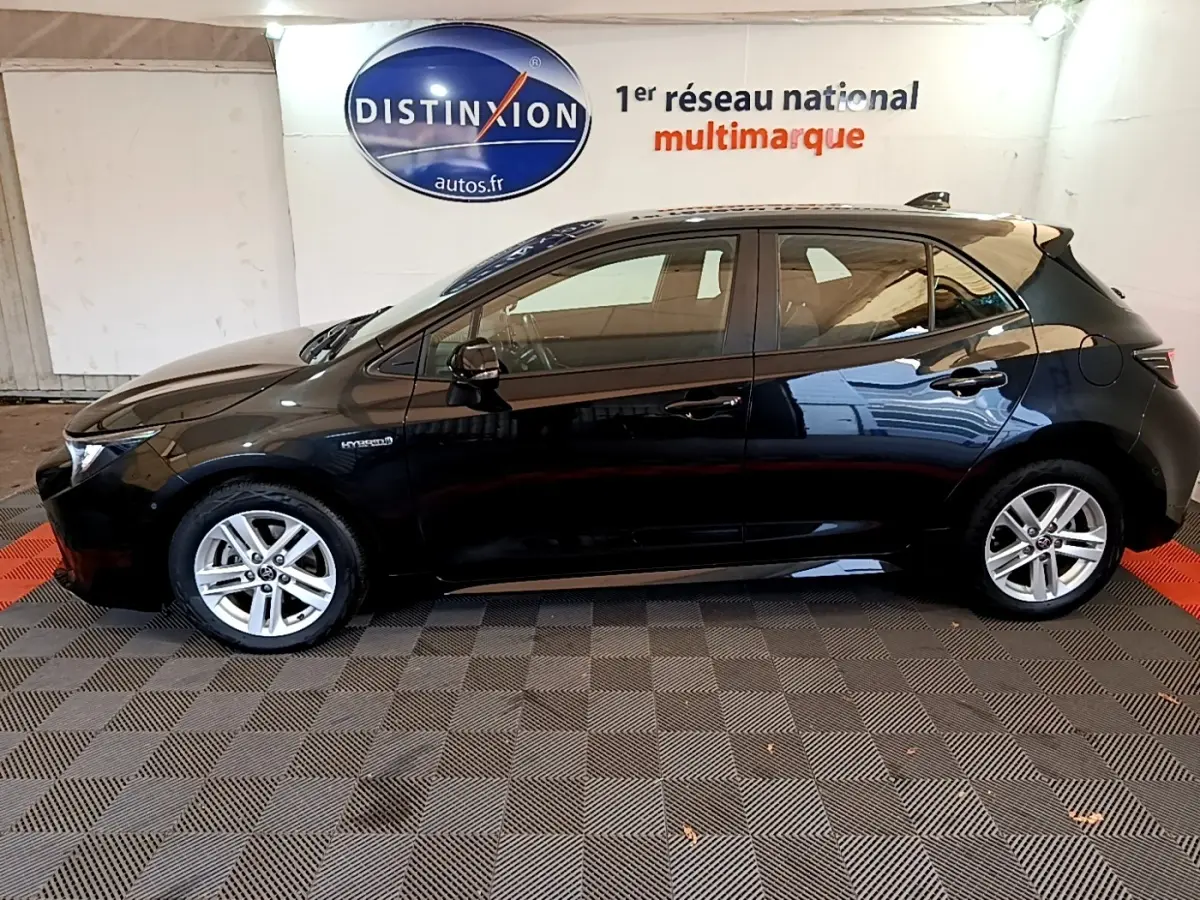 Profil côté gauche d'une Toyota Corolla hybride noire 2021, avec jantes alliage et badge Hybrid visible sur l'aile avant.