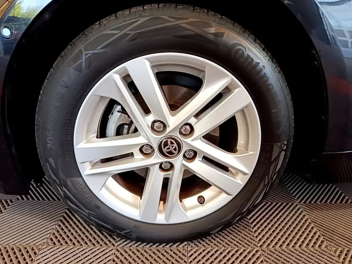 Gros plan sur la roue avant droite d'une Toyota Corolla noire, mettant en valeur la jante alliage et le logo Toyota central.