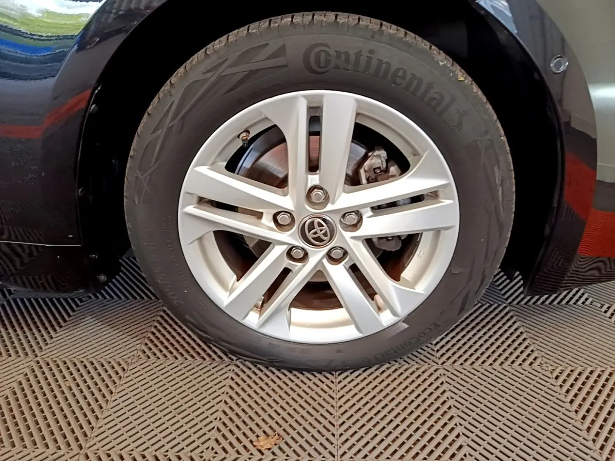 Gros plan sur la roue avant gauche noire de la Toyota Corolla hybride, avec jante alliage argentée et logo Toyota central.