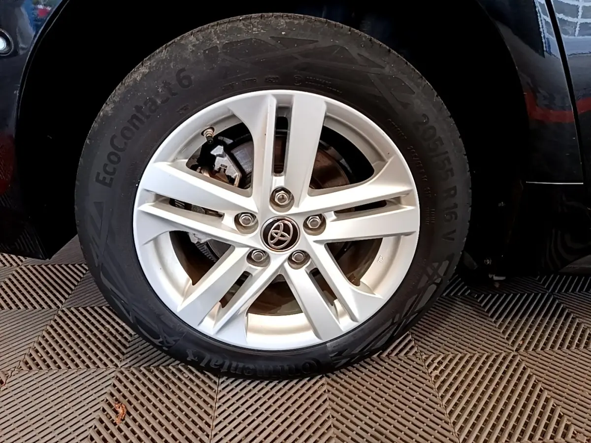 Gros plan sur la roue avant droite d'une Toyota Corolla noire, jante alliage argentée avec logo Toyota central.