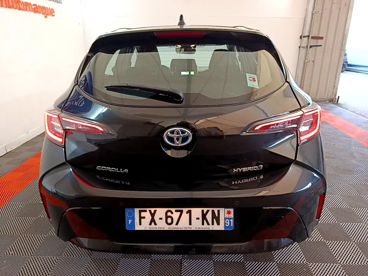 Vue arrière d'une Toyota Corolla hybride noire, avec feux LED allumés et plaque d'immatriculation française visible.