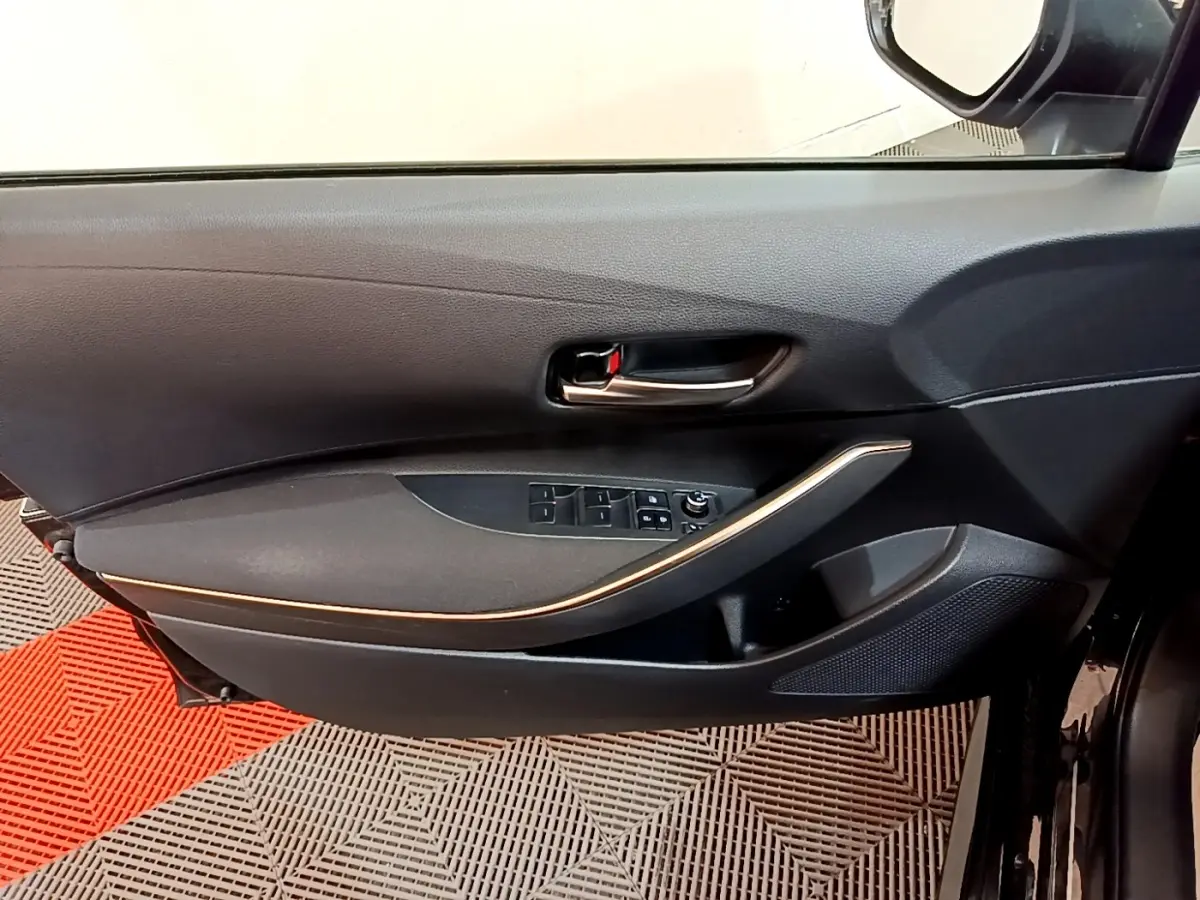 Vue intérieure côté gauche de la porte avant noire de la Toyota Corolla hybride avec commandes de vitres et poignée chromée.