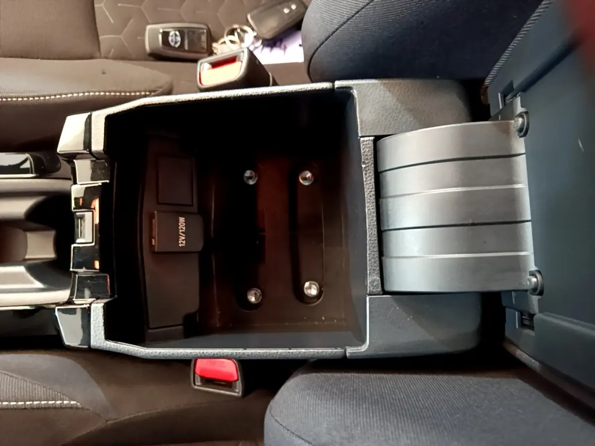 Vue plongeante sur le rangement central noir ouvert de la Toyota Corolla hybride 2021, montrant prise 12V et console entre sièges.