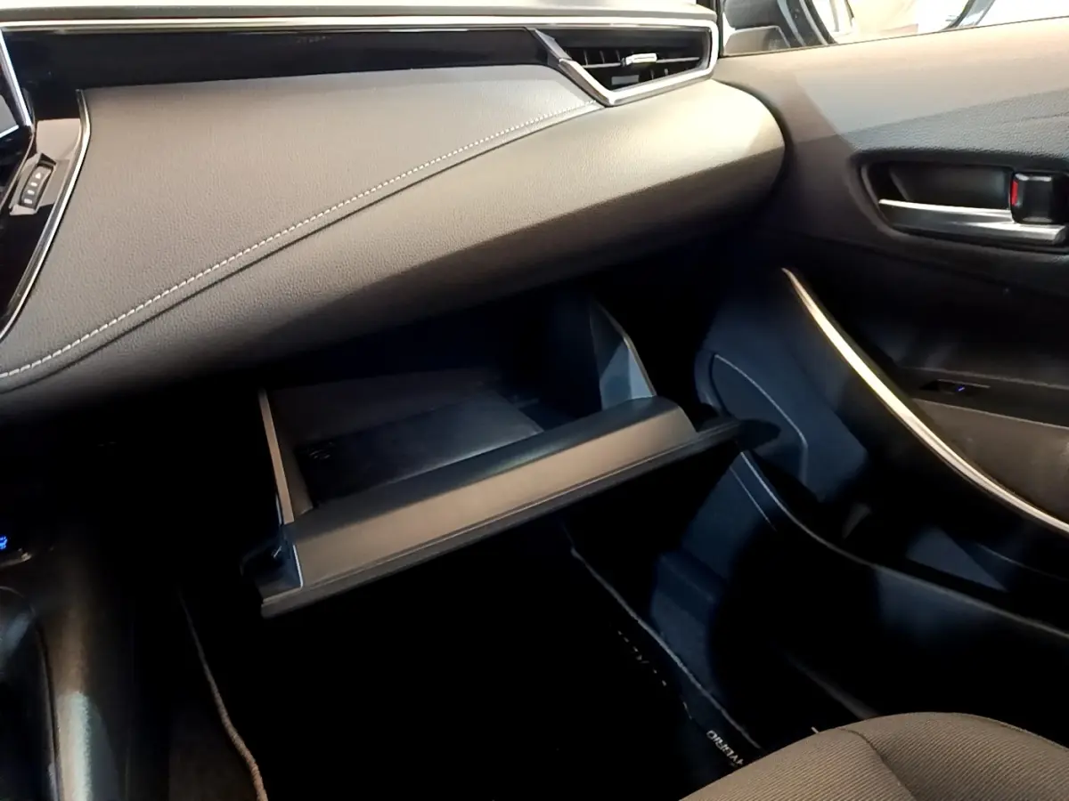 Intérieur côté passager de la Toyota Corolla hybride 2021, boîte à gants ouverte et tableau de bord noir avec surpiqûres blanches.
