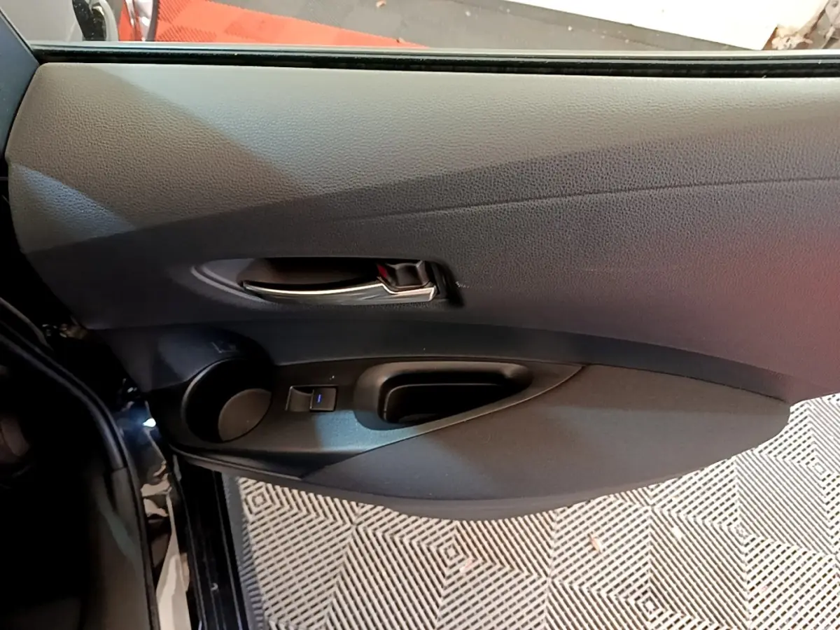 Intérieur côté gauche de la porte noire d'une Toyota Corolla Hybride 2021 avec poignée argentée et commande de vitre.