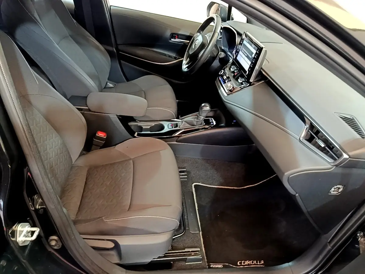 Intérieur noir vu côté passager avant de la Toyota Corolla hybride 2021 avec tableau de bord moderne et écran tactile.