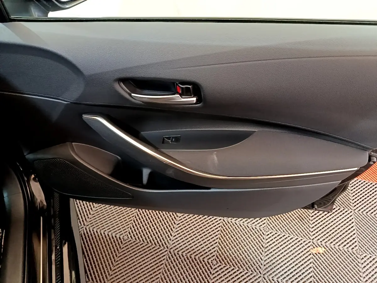 Gros plan sur la porte intérieure côté conducteur noire de la Toyota Corolla hybride 2021 avec poignée chromée et garniture argentée.