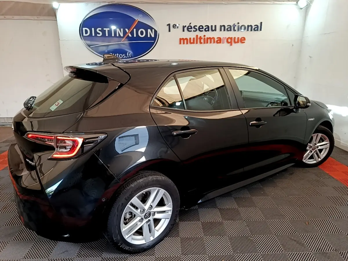 Toyota Corolla hybride noire vue 3/4 arrière droit en intérieur avec feux arrière LED et jantes alliage.
