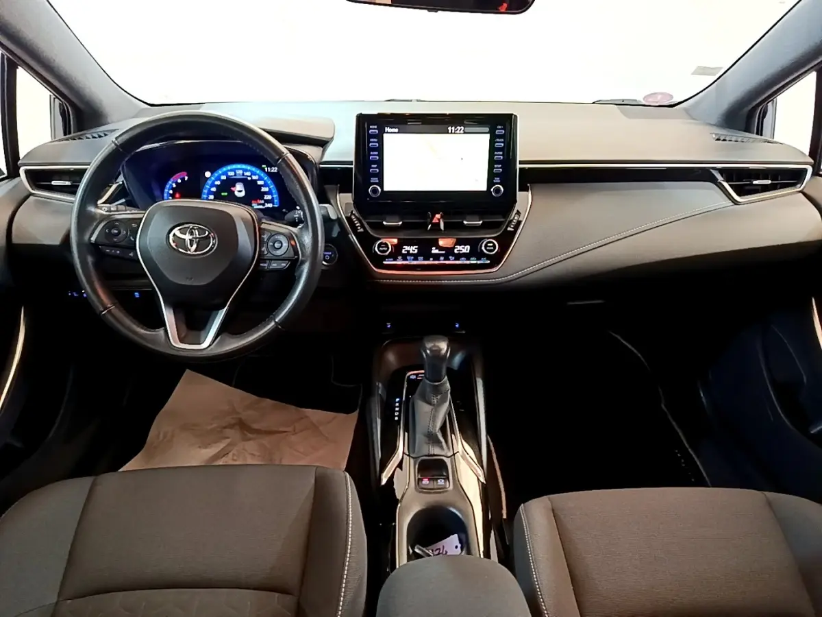 Intérieur noir de la Toyota Corolla hybride 2021, vue frontale du tableau de bord avec écran tactile et volant multifonctions.