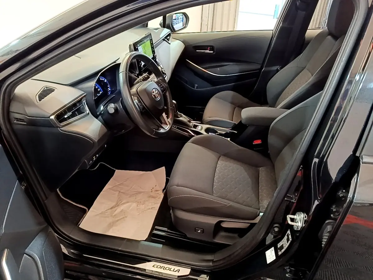 Intérieur noir de la Toyota Corolla hybride 2021 vu côté conducteur, avec tableau de bord et écran tactile visible.