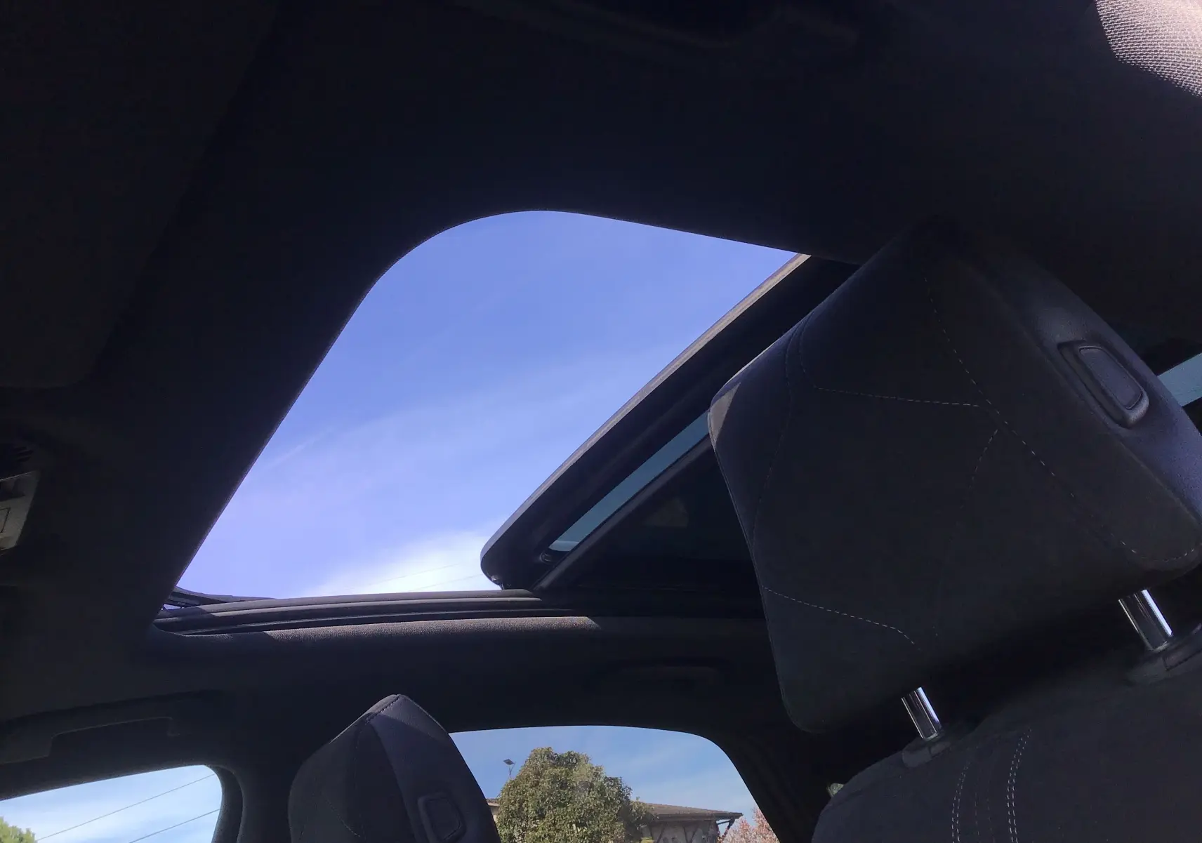 Vue intérieure du toit ouvrant panoramique et appuie-tête avant du DS7 Crossback noir, sous un ciel bleu clair.