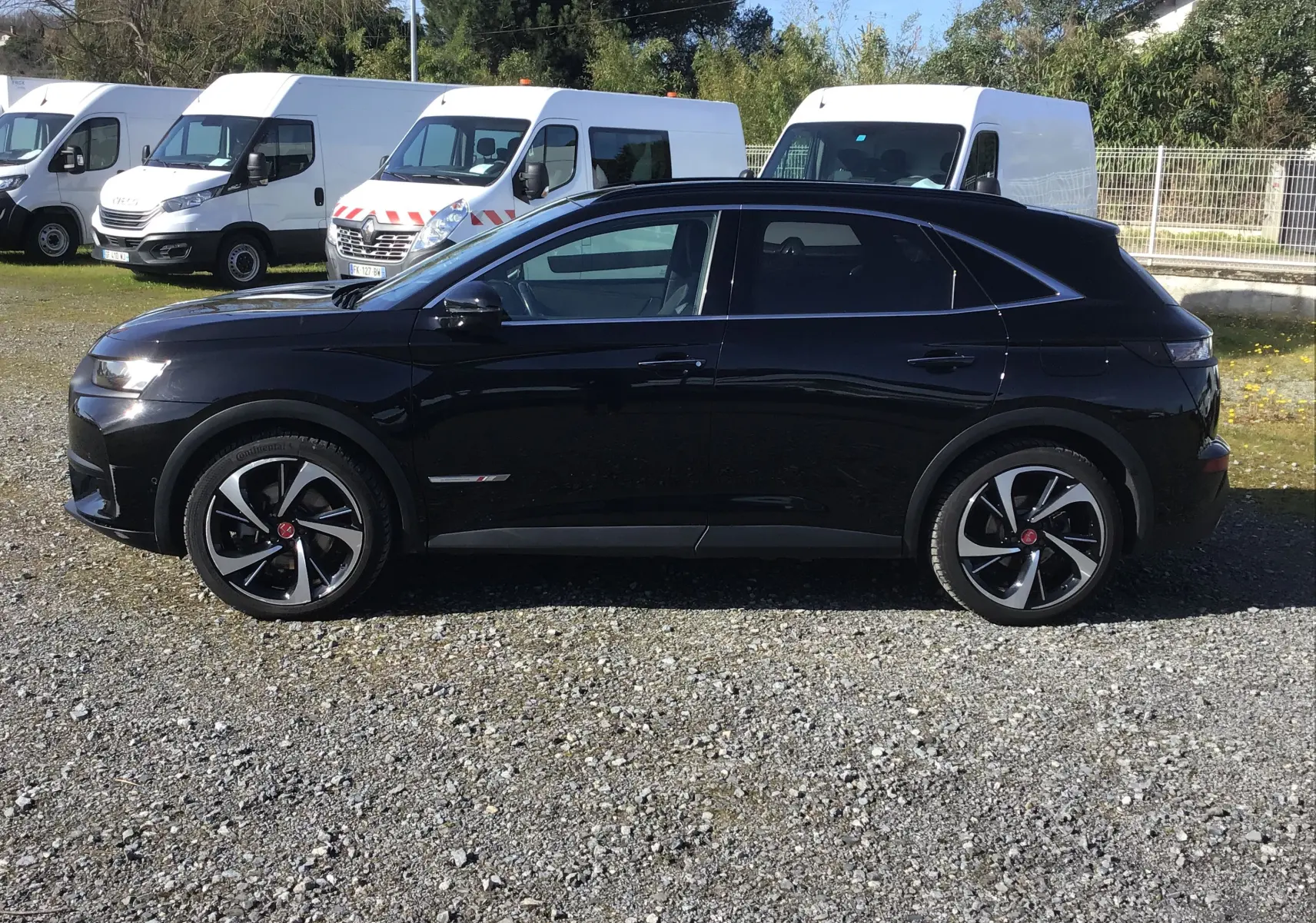 Vue de profil côté gauche d’un DS7 Crossback noir 2023 avec jantes alliage noires et chromées sur un sol gravillonné.