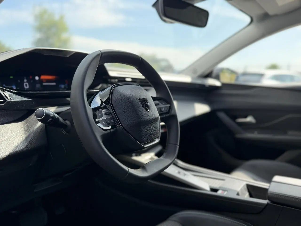 Intérieur de la Peugeot 308 SW 2025 vu côté conducteur, volant cuir noir avec logo Peugeot au centre.
