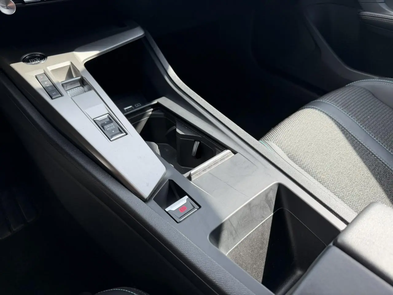 Vue rapprochée de la console centrale grise du Peugeot 308 SW 2025 avec levier de vitesses automatique et accoudoir tissu gris.