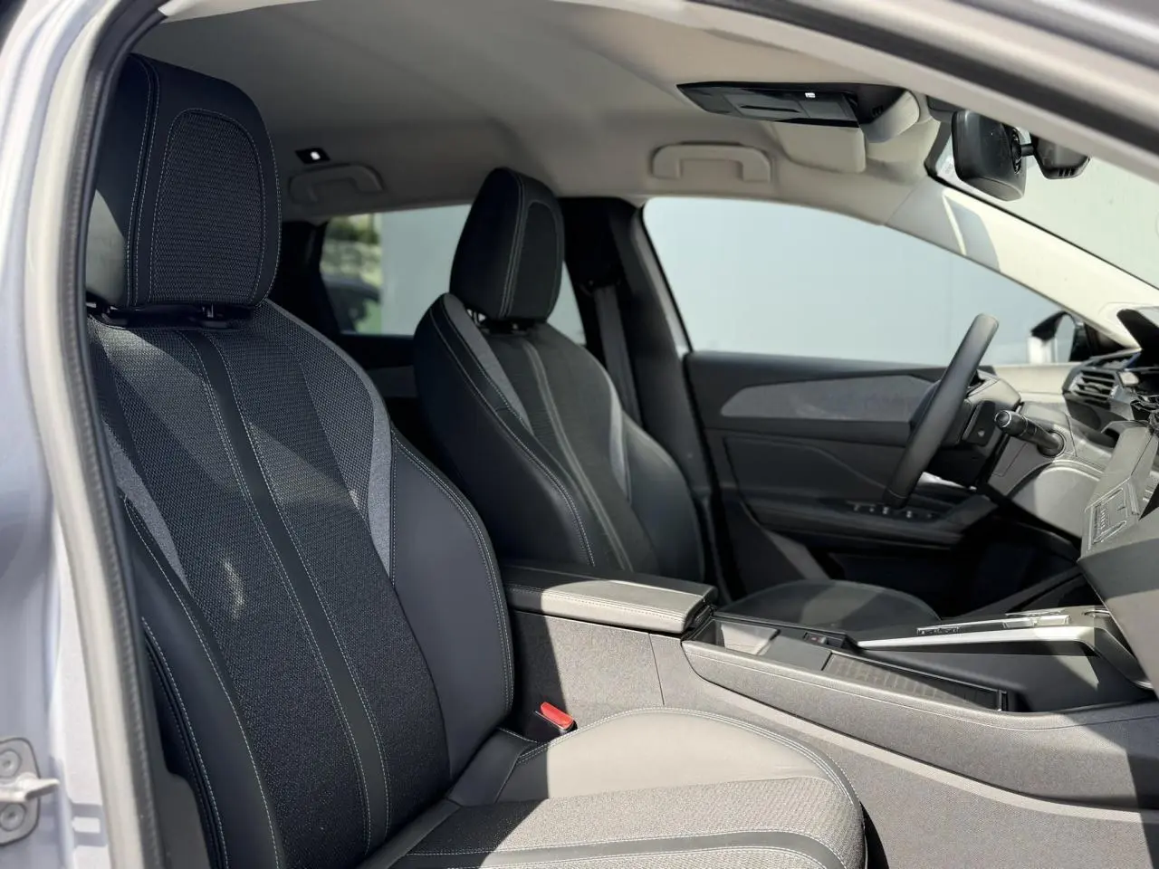Vue intérieure côté conducteur de la Peugeot 308 SW 2025, montrant les sièges en tissu et cuir noir avec surpiqûres contrastées.