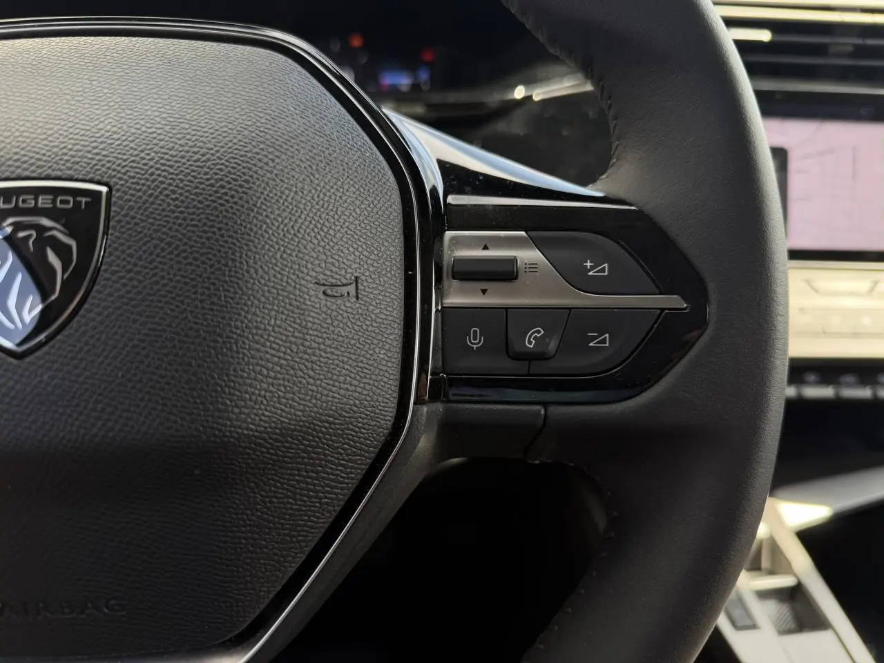 Gros plan sur le volant cuir noir du Peugeot 308 SW 2025 avec commandes audio et logo lion au centre.